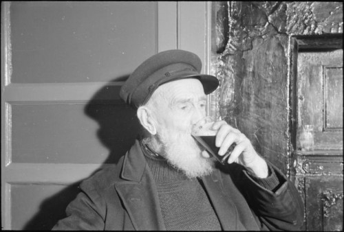 An elderly bearded man drinking beer.