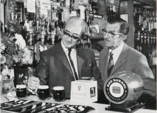 1970s photograph of two men in horn-rimmed glasses inspecting beer.