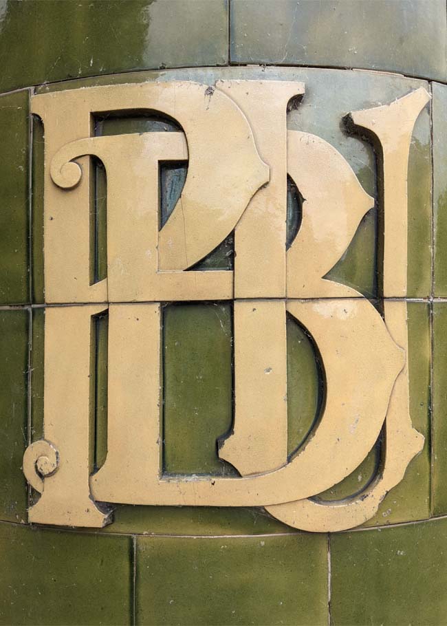 The letters P, B and U intertwined, in cream and green ceramics