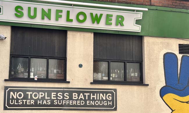 The exterior of The Sunflower with a green sign and a notice that reads "No topless sunbathing - Ulster has suffered enough".