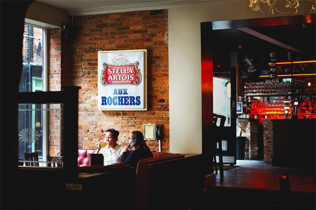 The interior of the Strait and Narrow with dark corners, red light and Belgian beer signs on the bare brick walls.