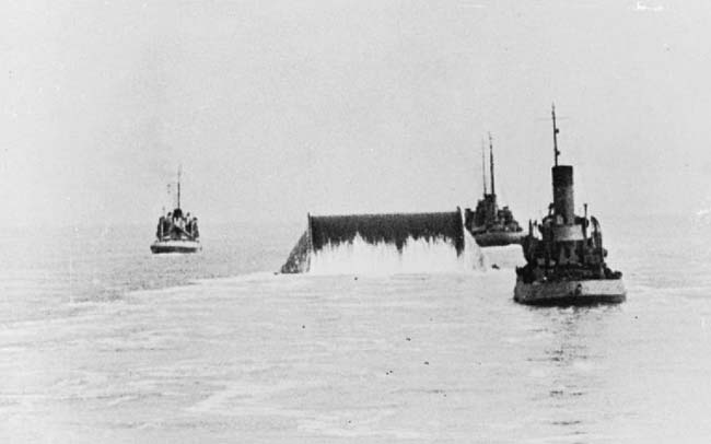 A black and white photo of small boats laying a pipeline in the English Channel.