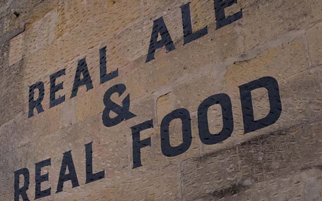 A painted sign on a pub wall: real ale and real food.
