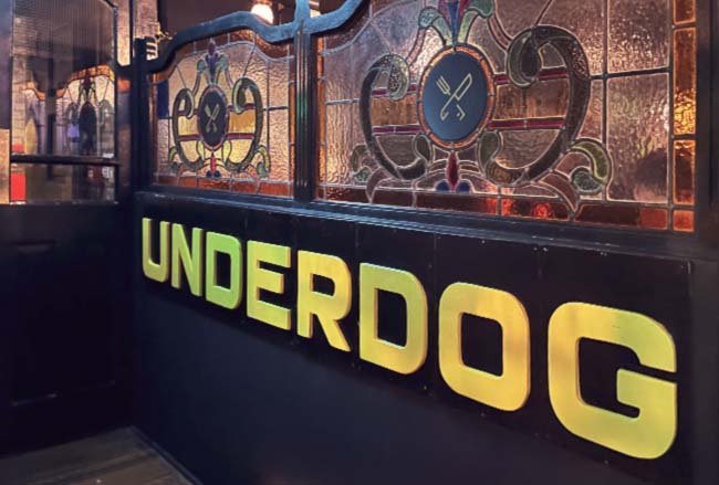 A big yellow sign for UNDERDOG on a pub wall.