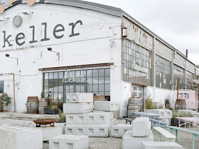 A white-painted industrial building with the logo of Mikkeller on the wall.