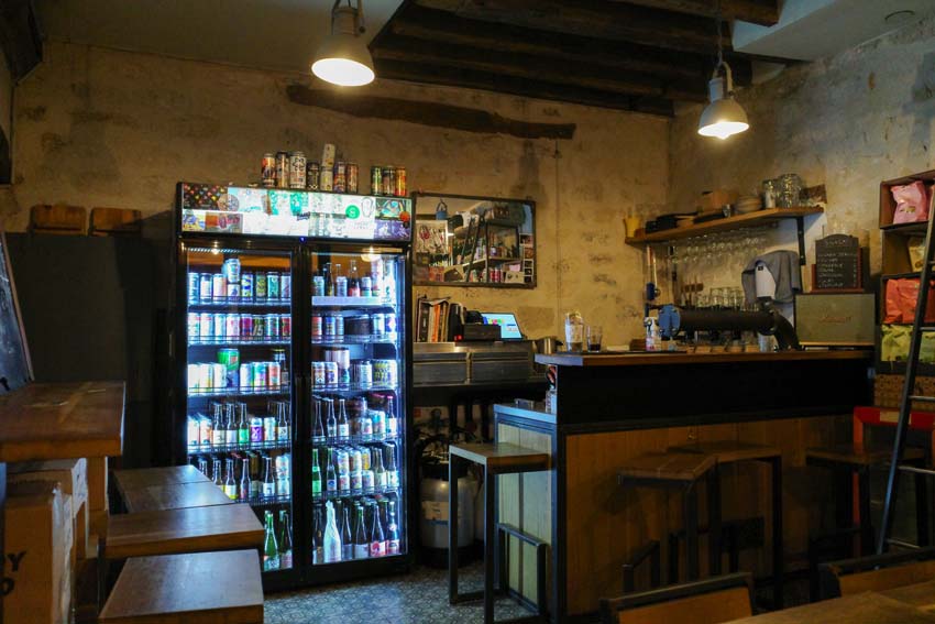The interior of BEER Paris with fridges full of cans, a small bar, and snacks hanging on the walls.