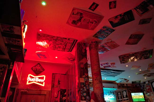 The neon lit interior of the Troll Café with Budweiser sign, Vedett sign and various posters and flags.