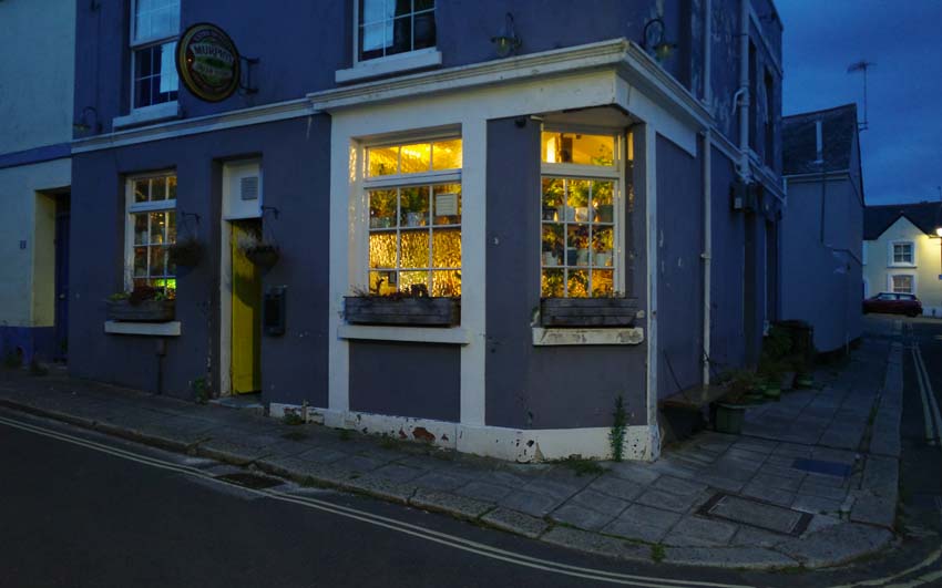The exterior of a corner pub with a glowing yellow window.