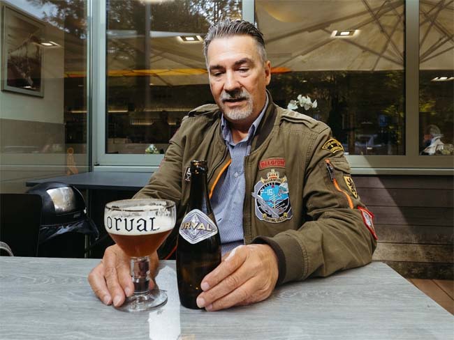 Stu Stuart, with neat grey hair and goatee, in a very American flying jacket with badges, contemplates a glass of Orval.