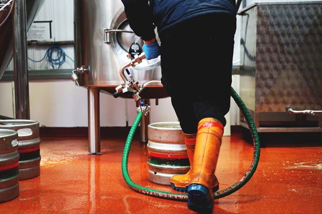 Someone in orange boots on an orange brewery floor transferring beer from a fermenting vessel, we think.