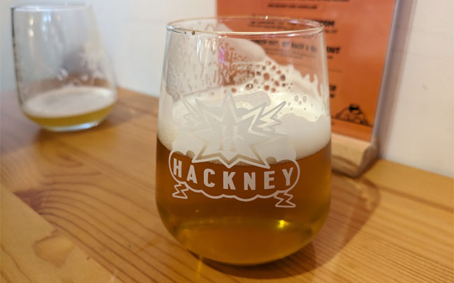 A tumbler of clear golden IPA with the Hackney Brewery logo.