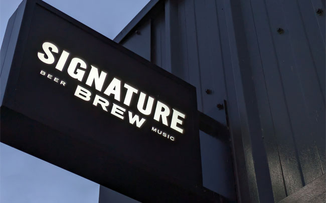 The illuminated sign for Signature Brew against a grey sky.