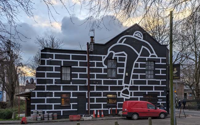 A Victorian pub with a mural of a person climbing over a brick wall in stark black and white.