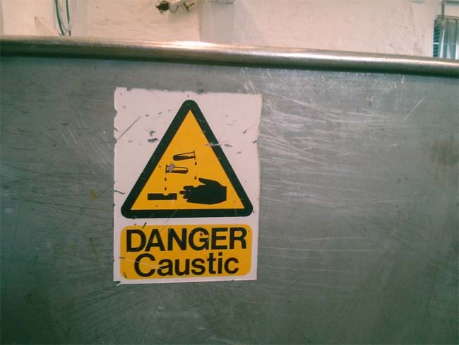 A warning sign on a brewing vessel: DANGER, CAUSTIC.